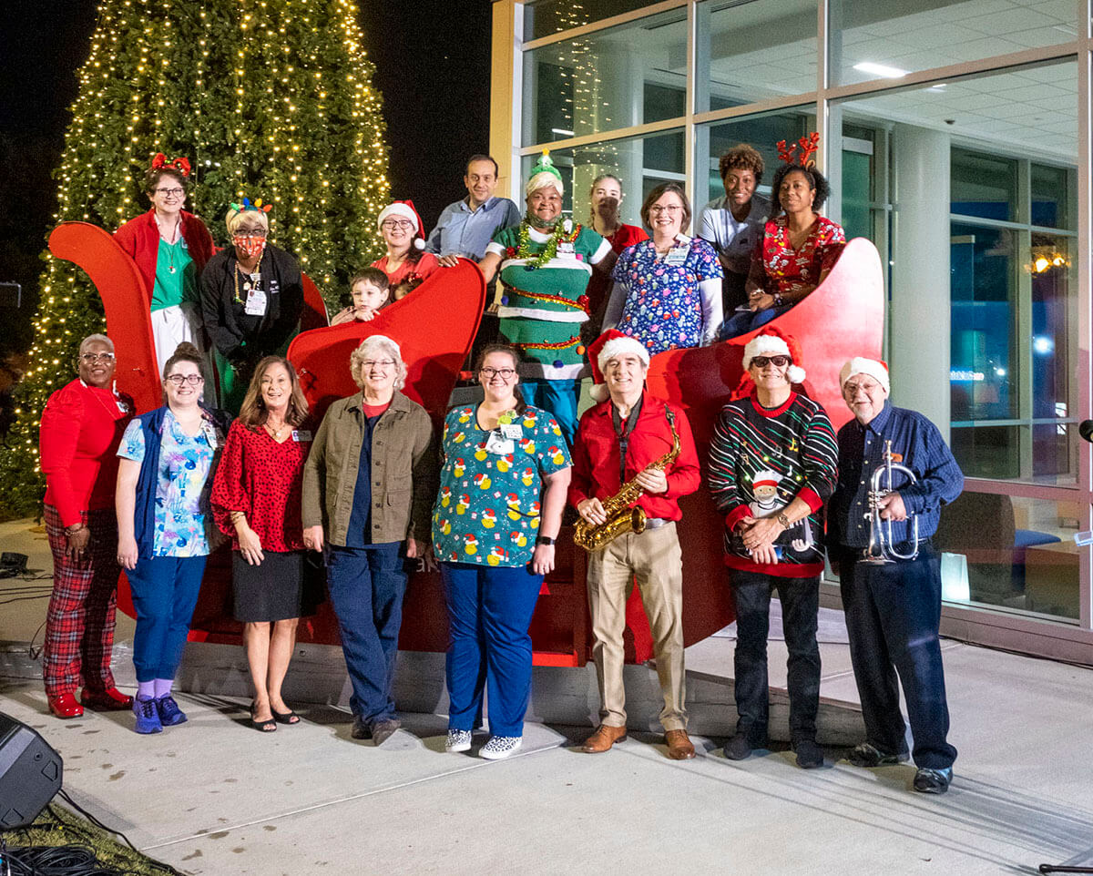 Atrium Health Navicent team members in Christmas themed clothes posing for a group photo at a tree lighting ceremony.