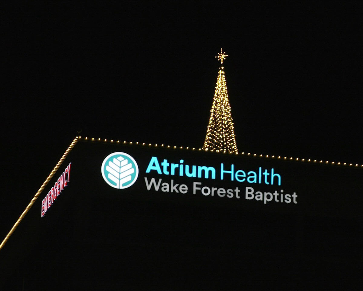 A Christmas tree with lights on top of the Atrium Health Wake Forest Baptist Davie building.