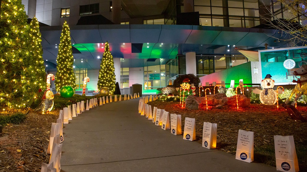 A walkway leading to Atrium Health Levine Children's Hospital adorned with Christmas tree lights, floats and luminaries.