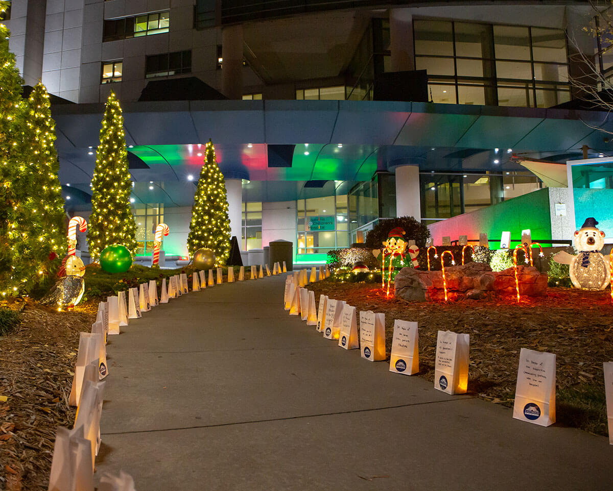 A walkway leading to Atrium Health Levine Children's Hospital adorned with Christmas tree lights, floats and luminaries.
