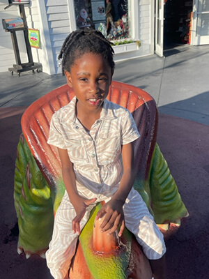 A young child sitting on a dinosaur and smiling at the camera.