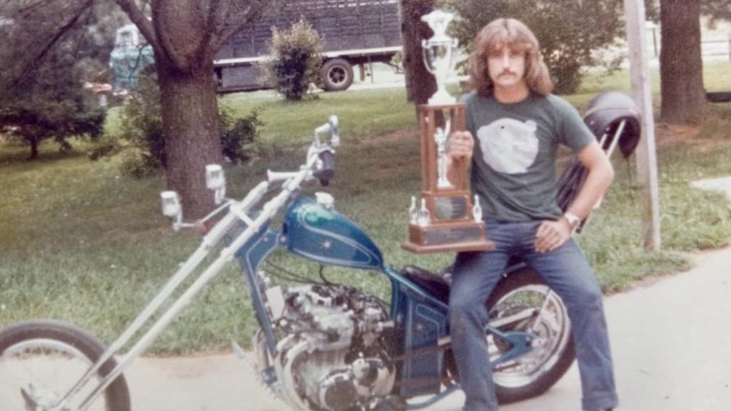 Curtis Whittington in a t shirt and jeans sitting on a motorcycle.