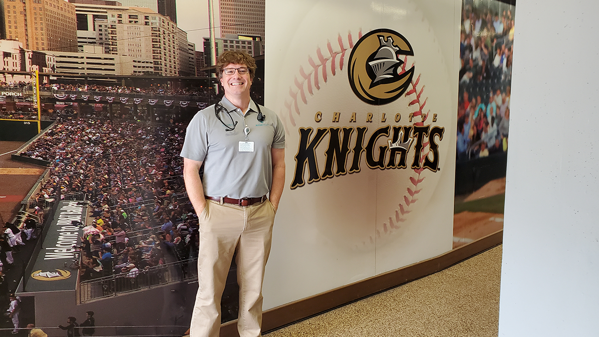 Dr. Eric Warren, sports medicine physician with Atrium Health Musculoskeletal Institute, stands in front of a photo wall at the Charlotte Knights stadium.
