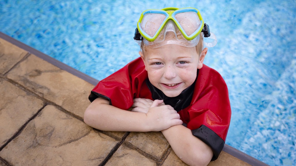 Oliver wearing a red shirt and goggles while swimming in a pool.