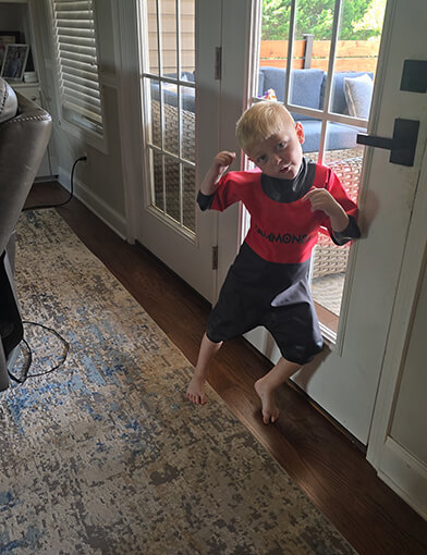 Oliver standing next to a door wearing a red and black wetsuit.