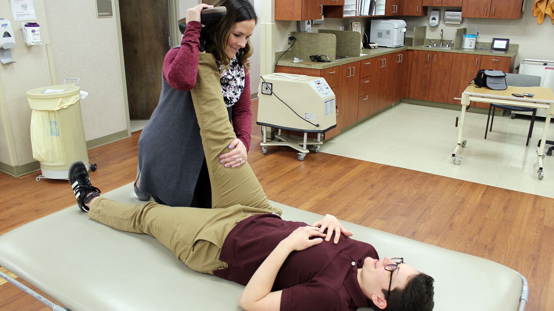 Colleen Theissen (on the table) and Lauren Van Laethem, exercise specialists at Carolinas Rehabilitation, demonstrate the proper way to perform a hamstring stretch with a partner. 