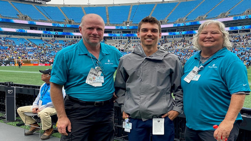 Two men and one woman on stadium sidelines in front of soccer field in Charlotte, NC representing the CLT Football Club.