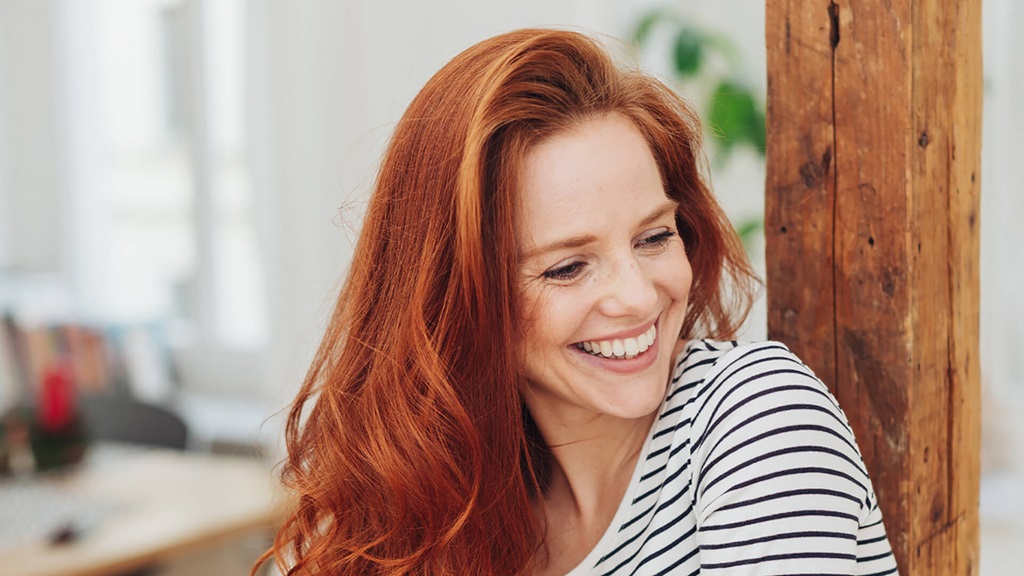 A woman with long red hair looking in the distance and smiling.