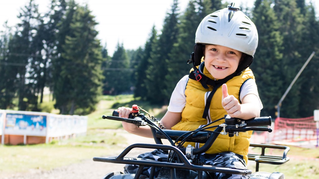 A young boy on an ATV while wearing a gray helpet and yellow vest.