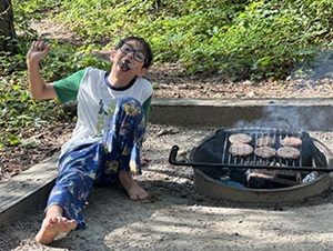 A child eating by a campfire.