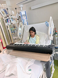 A child playing a piano in a hospital bed.