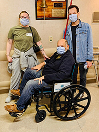 Two people standing behind a man in a wheelchair.