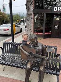 A baby standing beside a bronze statue.