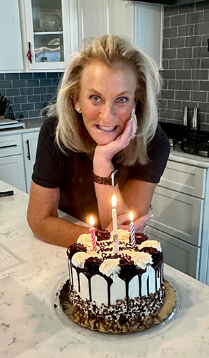 A person posing in front of a birthday cake.