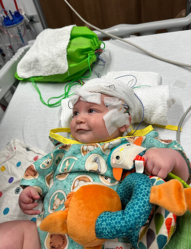 A baby resting in bed with a bandage on its head.