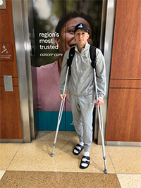 A man with crutches standing in front of a glass door.