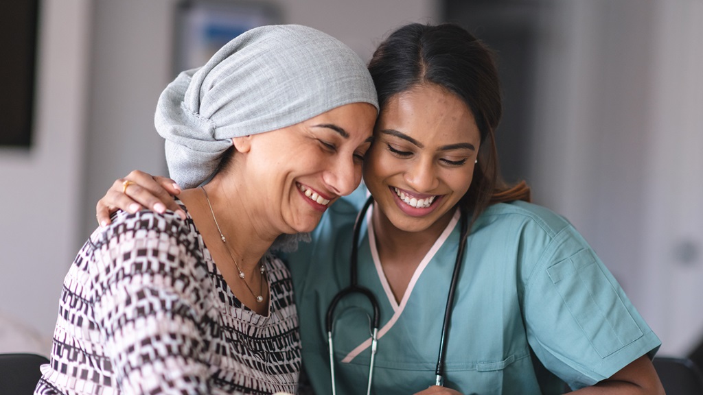 A woman in a black and white gown wearing a head covering smiles and speaks to a medical provider.