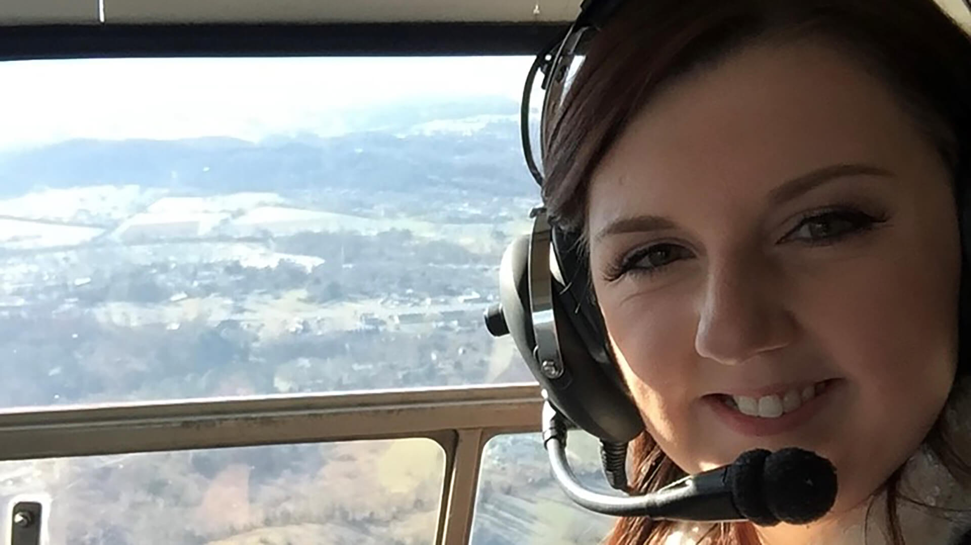 A young woman wearing a headset inside of a helicopter that is flying.