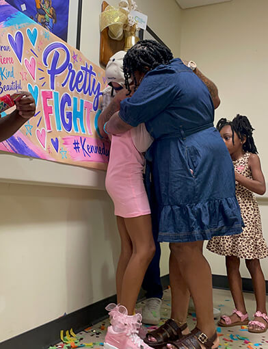 A young girl in pink hugging an older woman in a hospital.