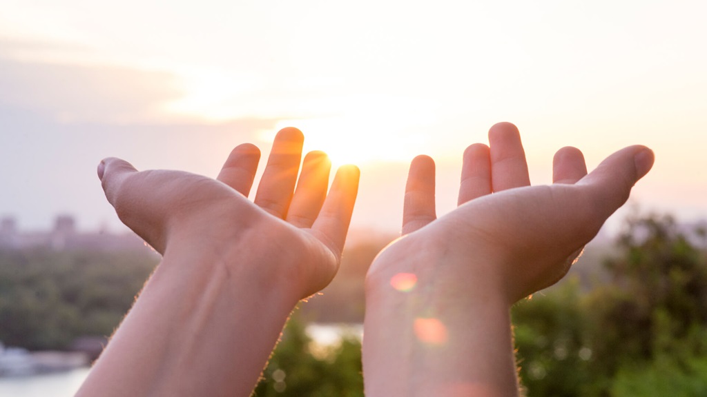 Hands reaching up toward the setting sun