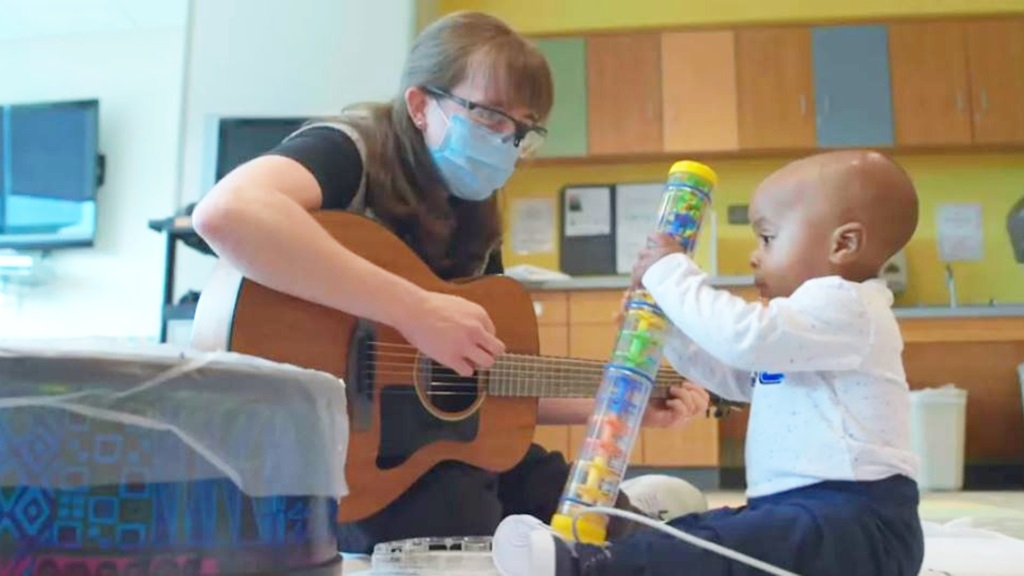 A music therapist plays guitar with a young Levine Children’s Hospital patient.