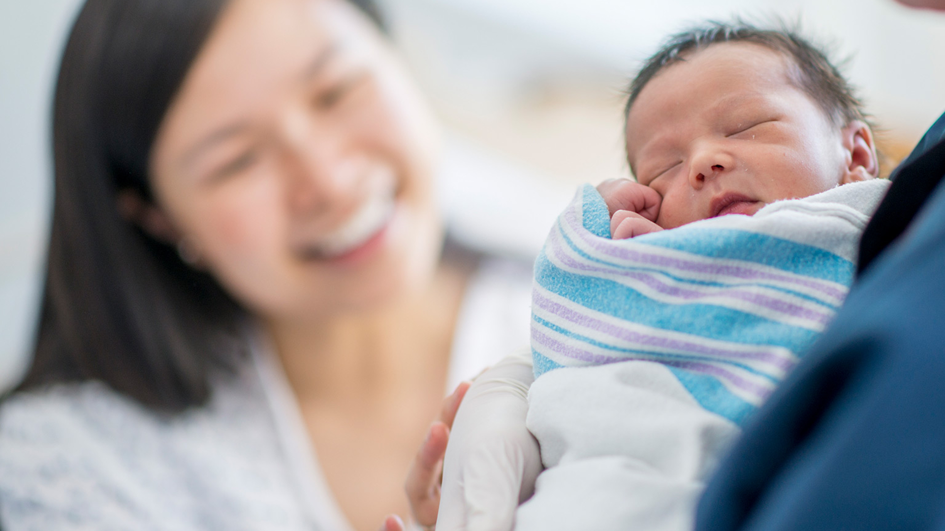 New mom smiling at baby held by nurse