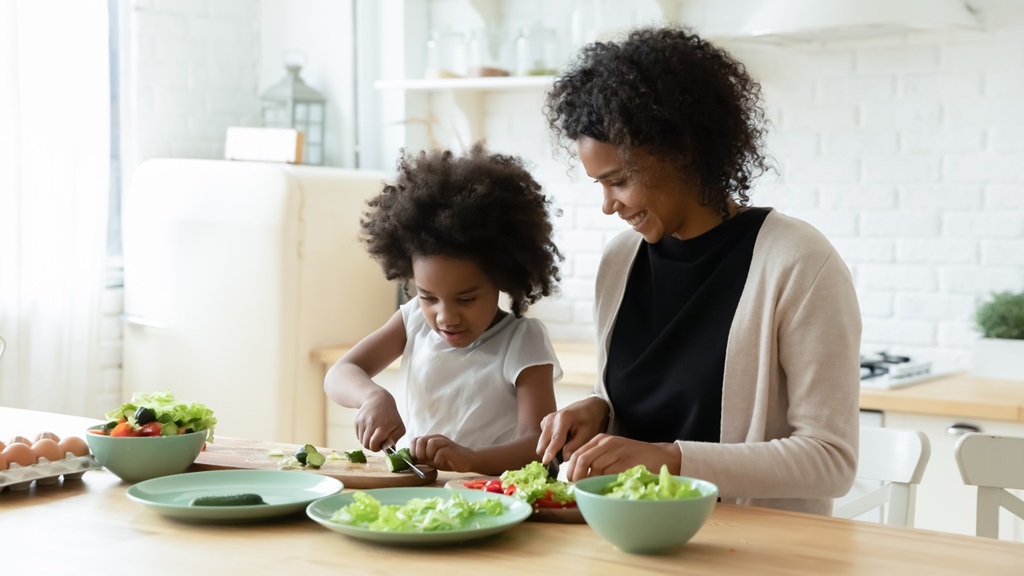Mother and daughter preparing salad in kitchen together.