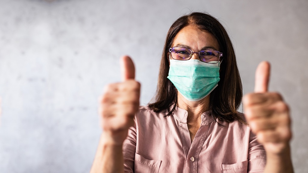 Woman with face mask on giving two thumbs up