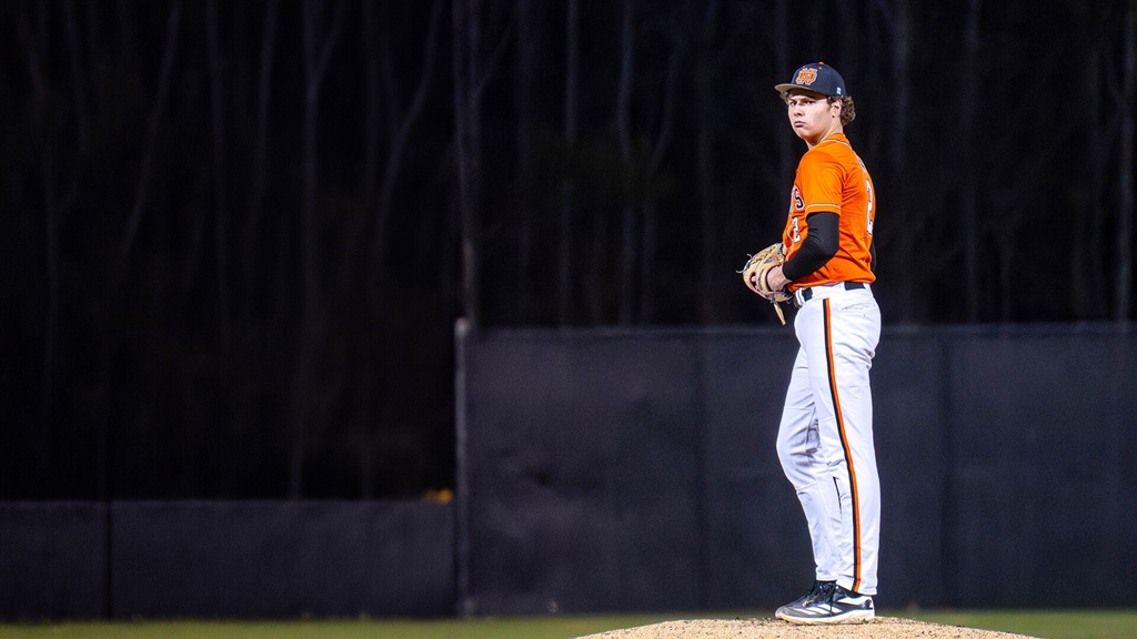 A baseball player in an orange jersey and white pants with a vertical stripe throwing a pitch during a game.