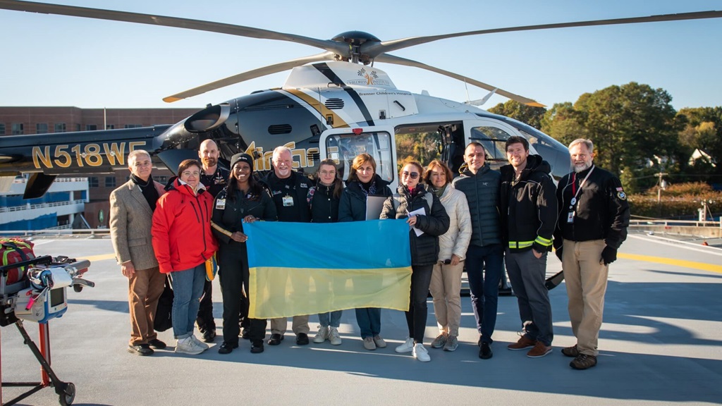 Group photo in front of helicopter with Ukrainian flag.