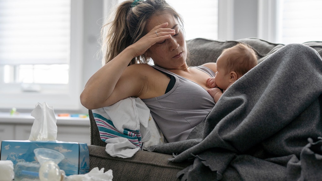 Mom on couch with baby and hand over eyes