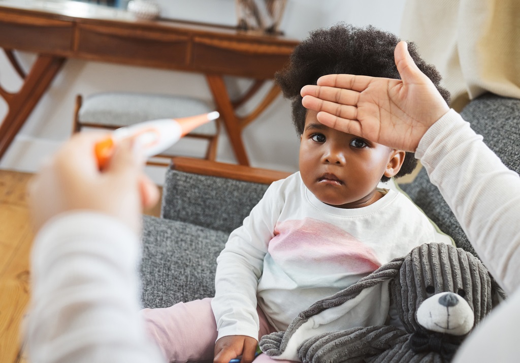 A child sitting on a couch with a hand over her forehead