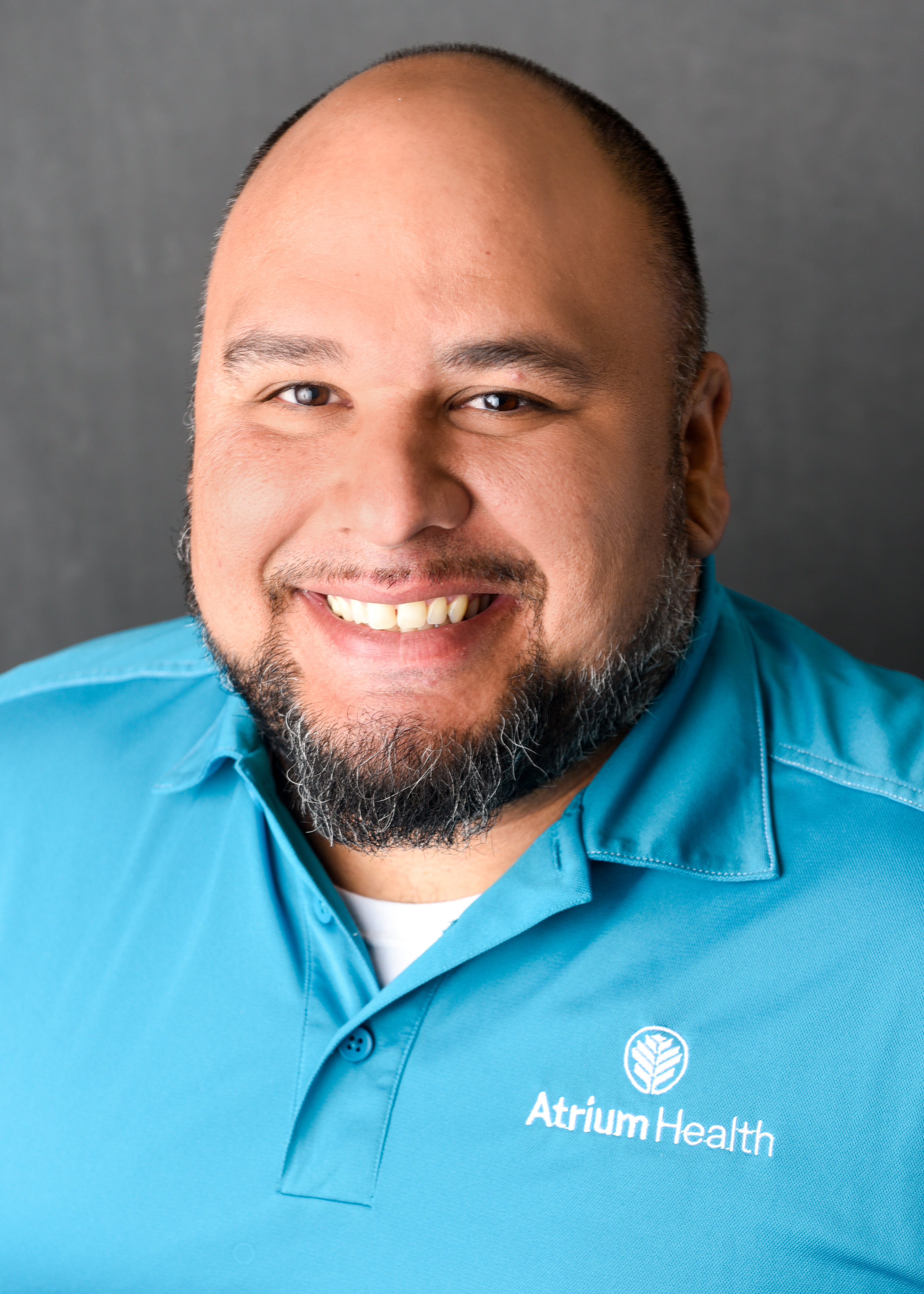 Headshot of a man smiling at the camera wearing a teal Atrium Health shirt