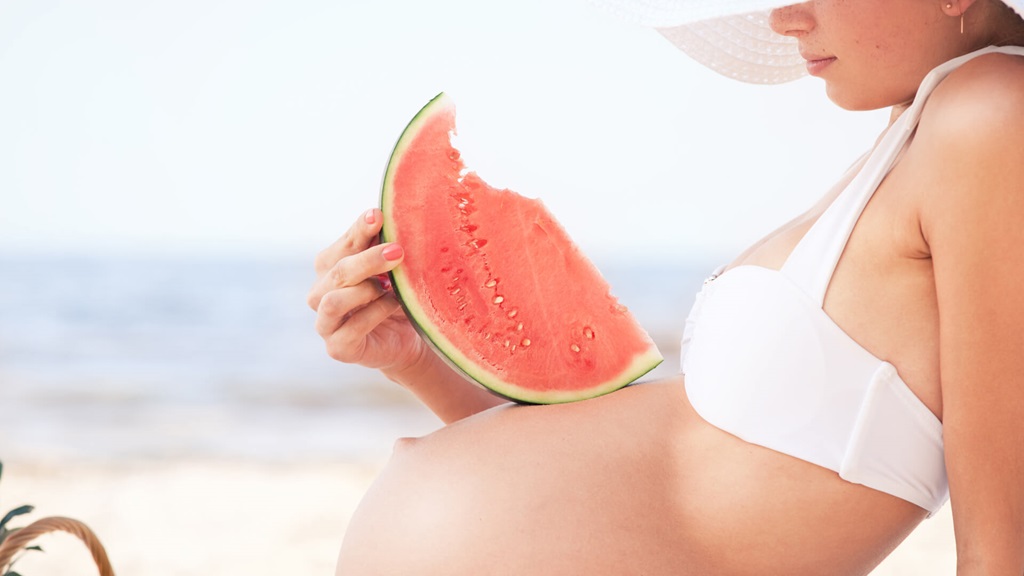 Pregnant woman on the beach with a watermelon slice on her belly