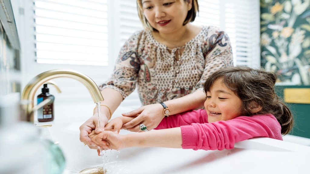 Child washing hands with the help of mom