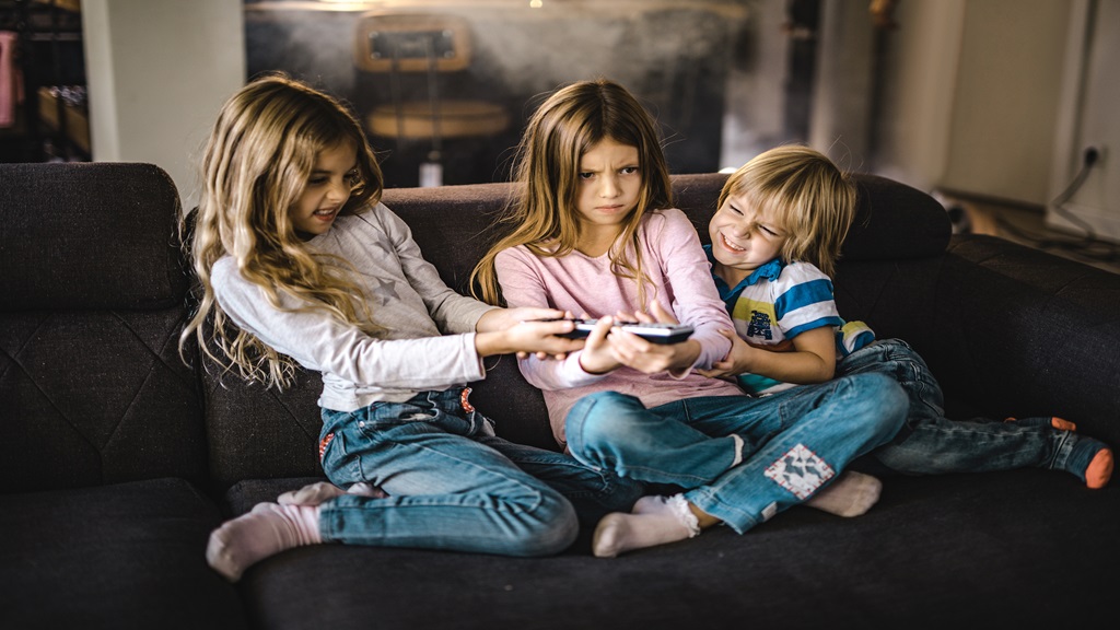 Three children tugging at a remote
