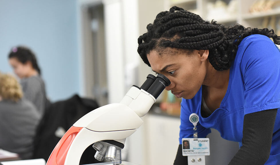 A woman in medical scrubs looking into a microscope.