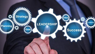 A man in a dark black suit pointing at a digital graphic consisting of several gears that say Leadership, planning, success and strategy.