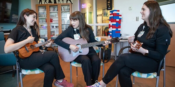A group of girls in black pants and shirts playing guitars and singing together.