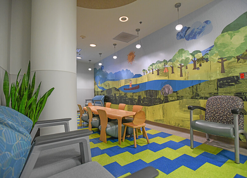 A hospital waiting room with a blue and green floor and a colorful landscape mural on the wall.